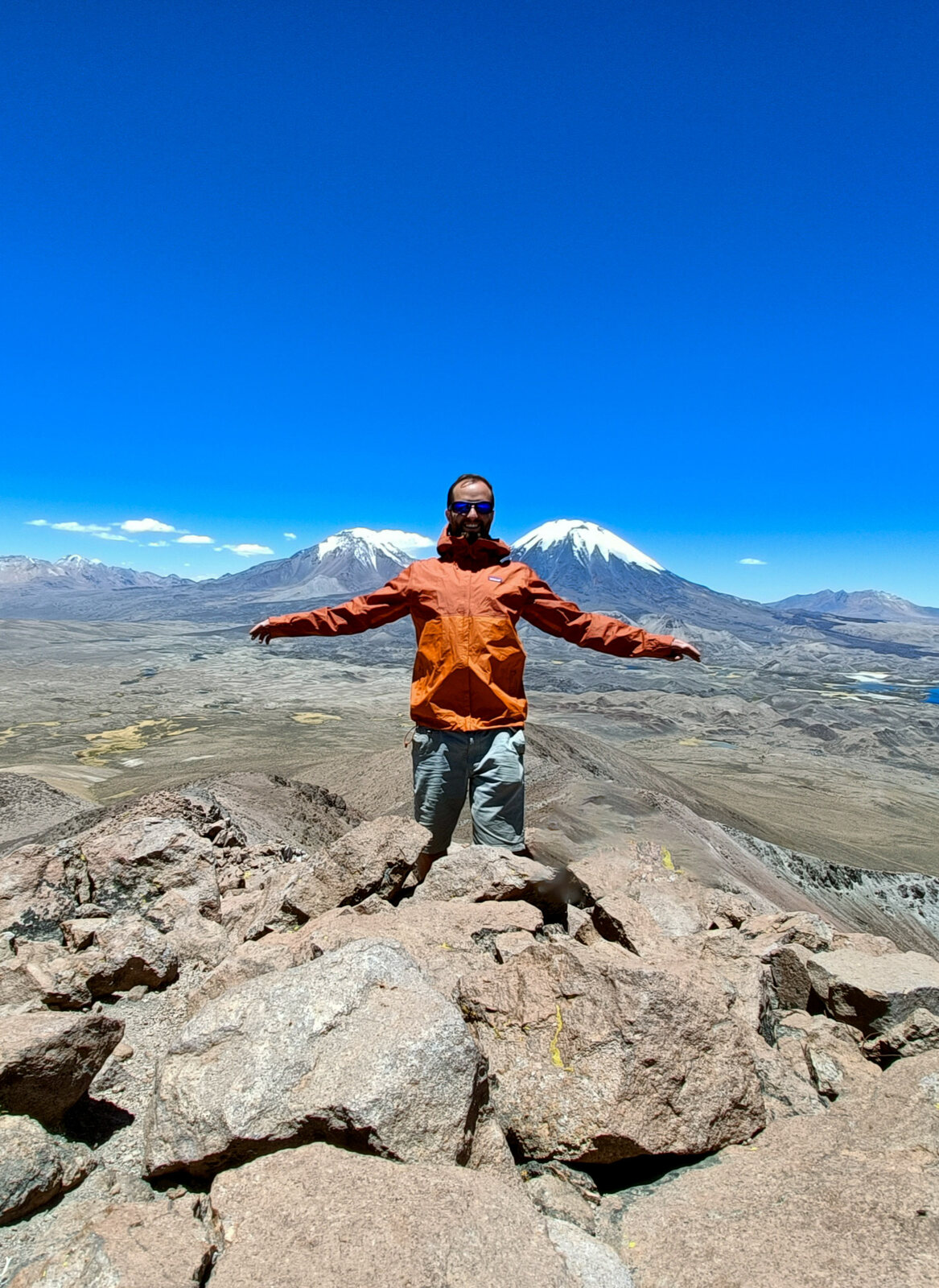 Arms open on a rock during acclimatisation, volcanoes behind